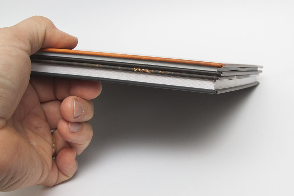 a 38 page non-layflat book (top) vs a 32 page layflat book (bottom) showing the difference in page thickness and overall book thickness